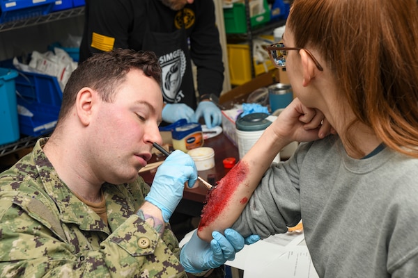 Hospital Corpman 2nd class Corey Boyd, field medical technician, applies moulage to a volunteer before a simulated training event at the Healthcare Simulation and Bioskills Center, on November 25, 2024. The joint training tested Sailors on the multiple stages of healthcare providing in an active combat zone.