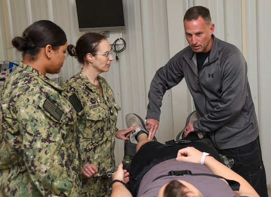 Lt. Cmdr. Michael Feroli, a physician assistant, right, conducts an exam on a simulated casualty during  a training event at the Healthcare Simulation and Bioskills Center, on November 25, 2024. The joint training tested Sailors on the multiple stages of healthcare providing in an active combat zone.