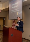 Deputy Under Secretary of the Navy (Policy) Advisor for International Affairs Phillip DeWolf delivers opening remarks at the NCIS Multiple Threat Alert Center Force Protection Intelligence Conference Nov. 19, 2024, at NCIS Headquarters.