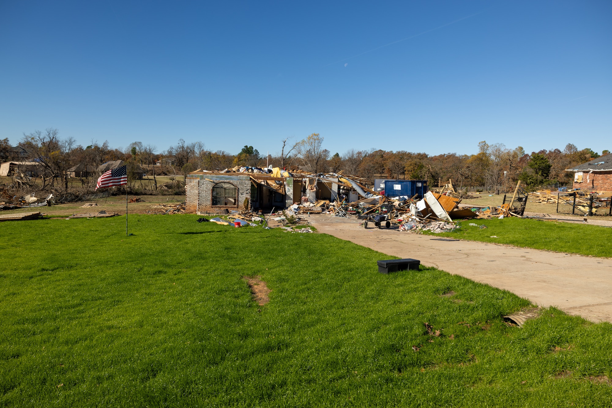 Photo of home damaged by tornado with American flag standing in yard.