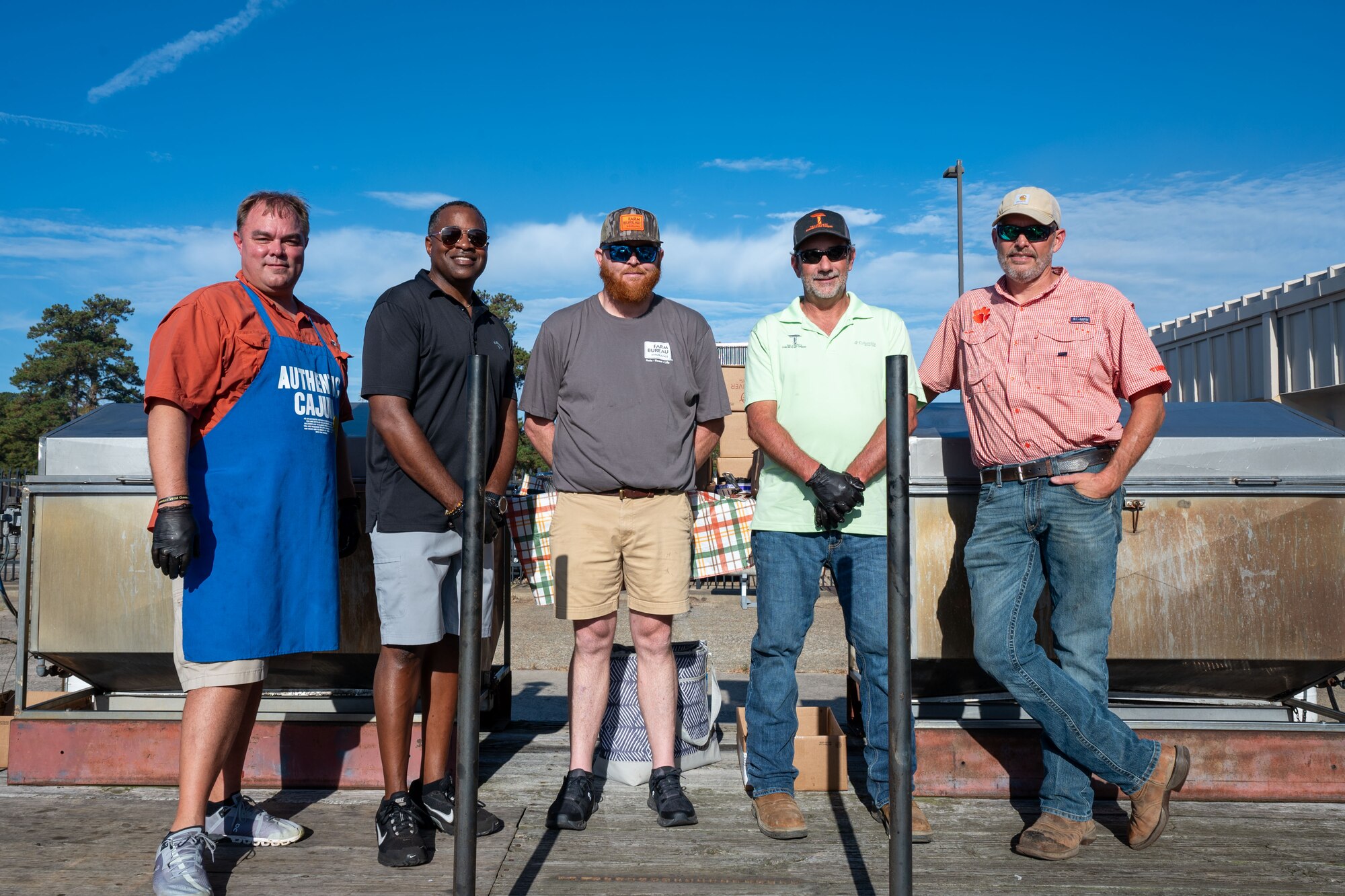 A group of men pose for a photo by a BBQ grill.
