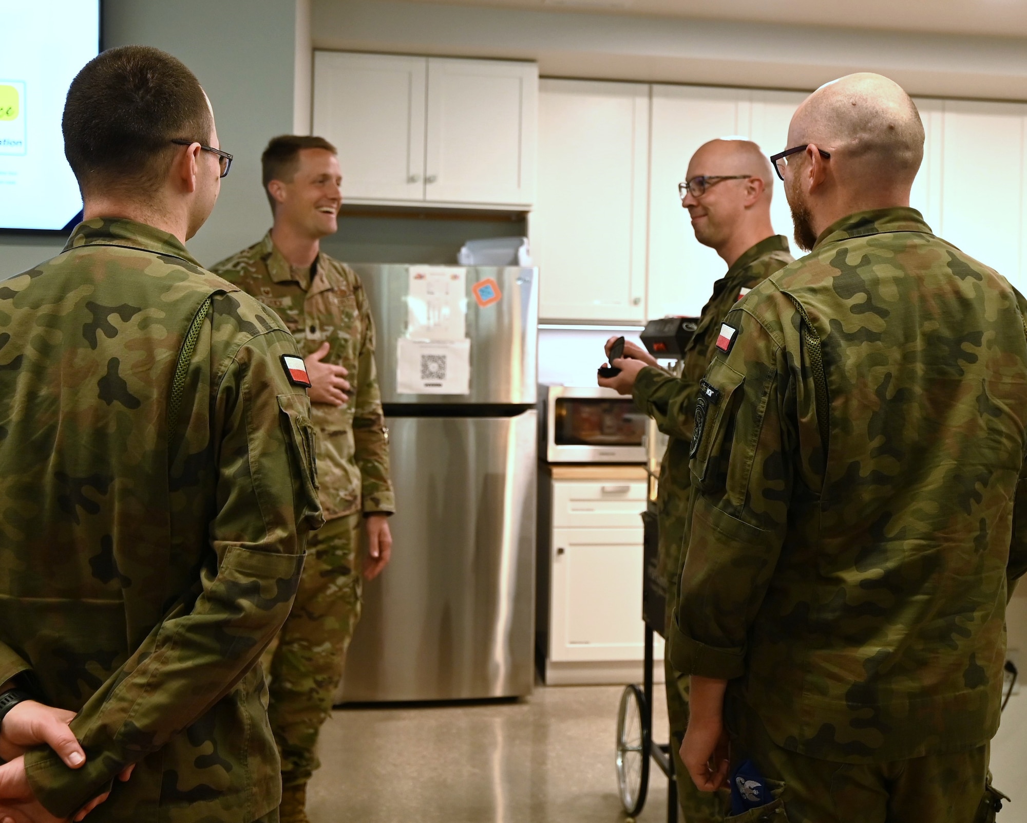 Polish and U.S. Air Force Airman stand in a breakroom and talk.