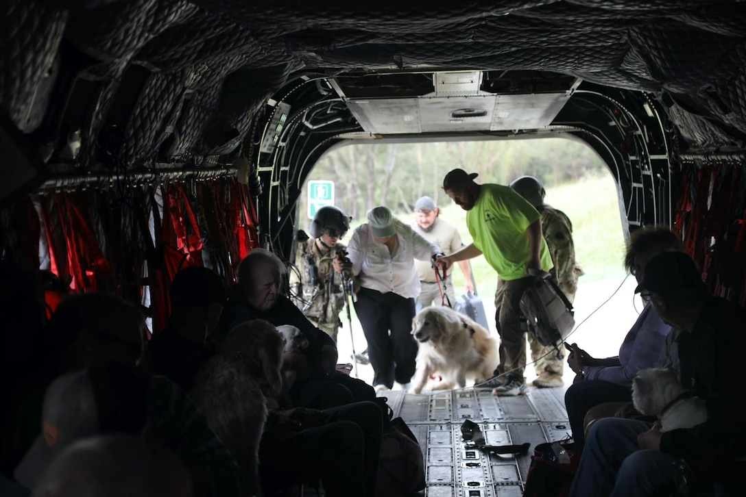 Soldiers help guide citizens, one with a dog, into a dark aircraft.