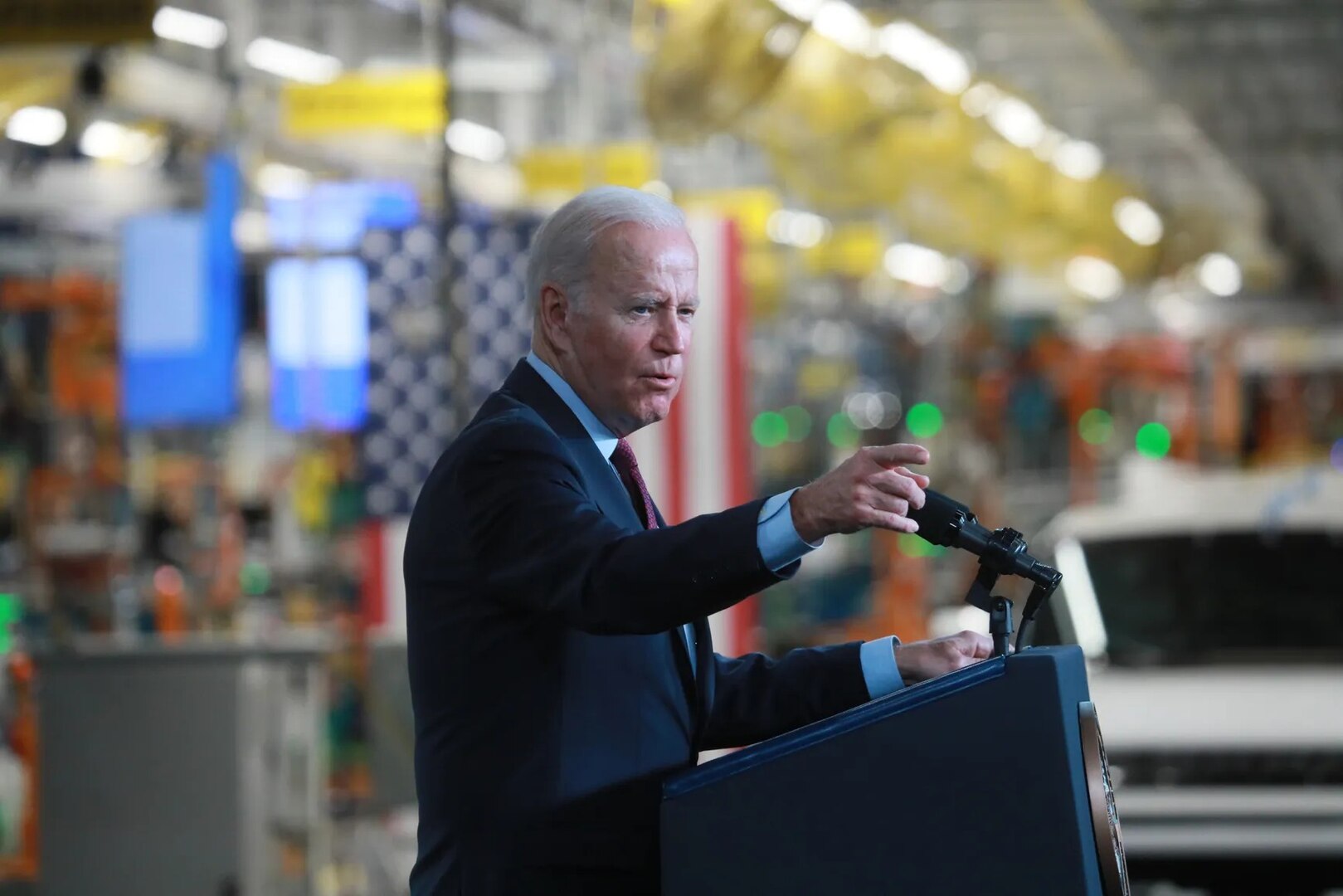 A man points from a podium in a factory.