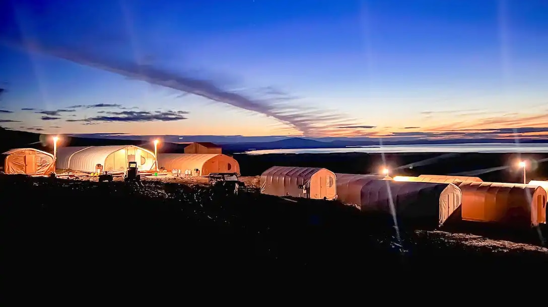 A group of tents are pitched on a hill during low light from the sun.
