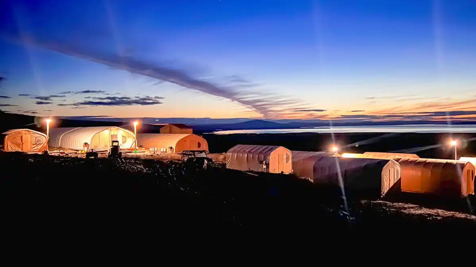 A group of tents are pitched on a hill during low light from the sun.