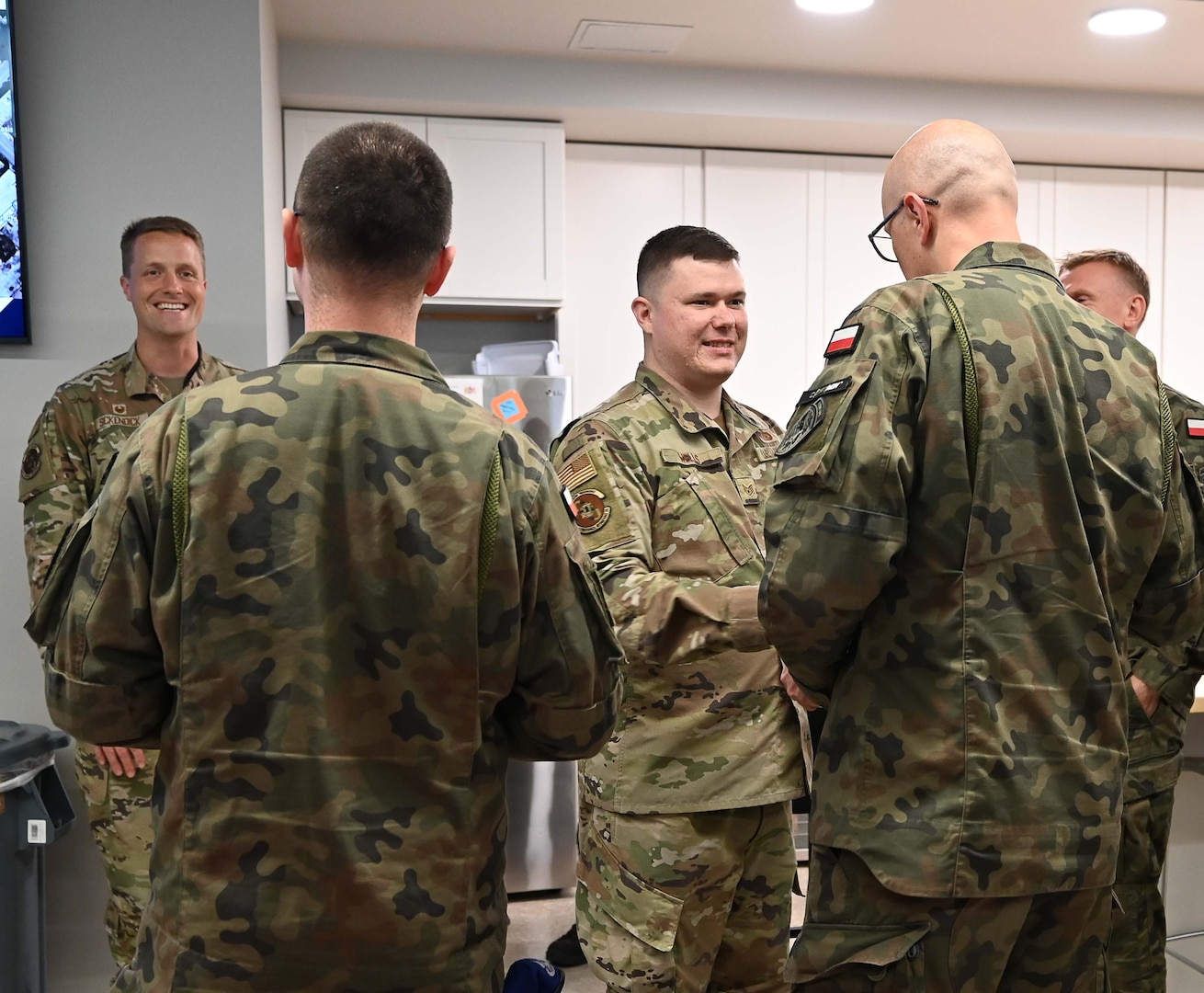 Polish and U.S. Air Force Airman stand in a breakroom and talk.