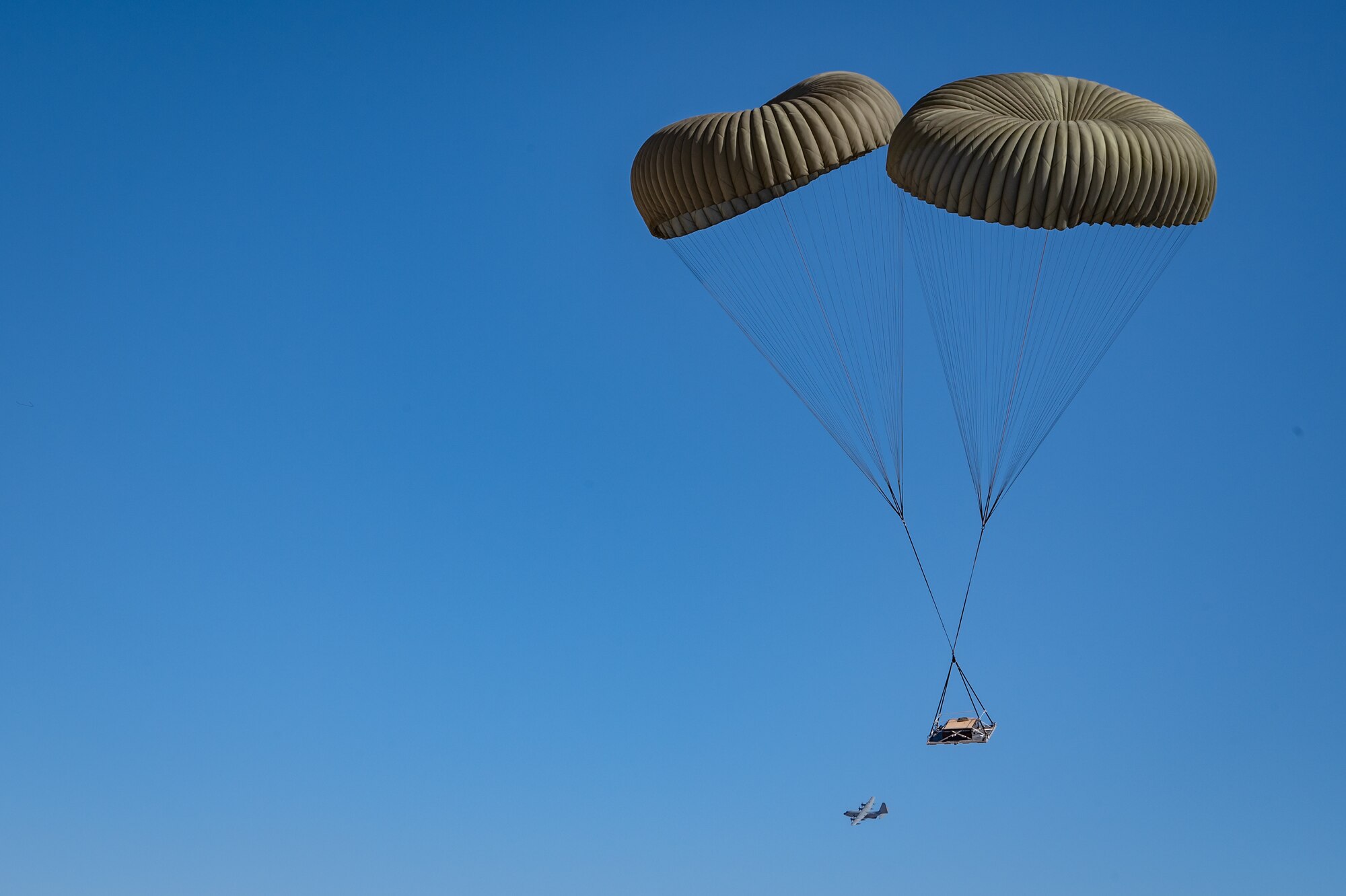 A cargo platform descends with the support of dual parachutes during Exercise Desert Hammer 25-1 at Auxiliary Airfield 6 near Gila Bend, Ariz., Nov. 14, 2024, as the U.S. Marine Corps KC-130J that dropped off the cargo departs in the background. This large-scale exercise showcases the adaptability of Mission Ready Airmen, advancing the skills needed to thrive in the rapidly evolving challenges of global competition. (U.S. Air Force photo by Tech. Sgt. Tyler J. Bolken)