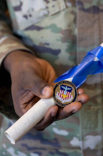 An Airman shows his coin and diploma