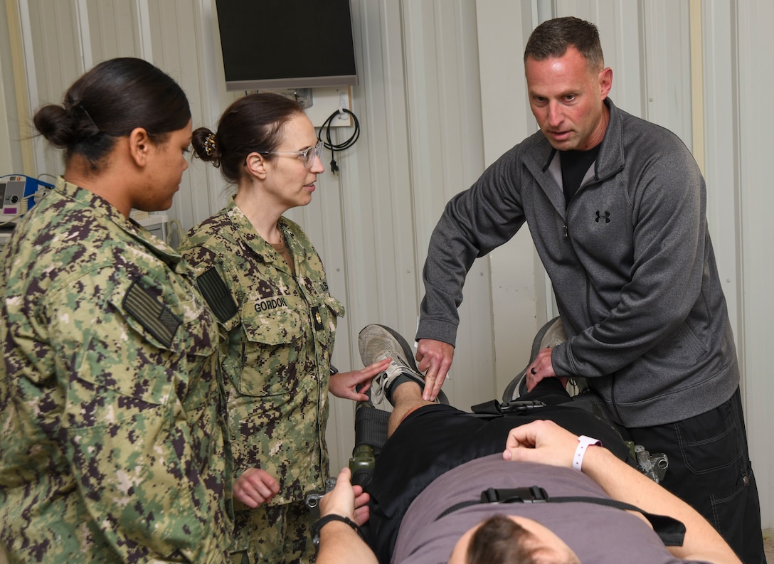 Lt. Cmdr. Michael Feroli, a physician assistant, right, conducts an exam on a simulated casualty during  a training event at the Healthcare Simulation and Bioskills Center, on November 25, 2024. The joint training tested Sailors on the multiple stages of healthcare providing in an active combat zone.