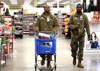 Two Soldiers walk through the Post Exchange while pushing a blue shopping cart.