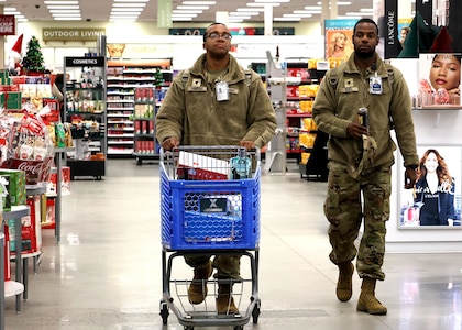 Two Soldiers walk through the Post Exchange while pushing a blue shopping cart.