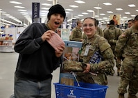 Two women, one in Army uniform and the other in black hat and sweat shirt, hold a clutch purse with smiling expressions after she had just won the purse from the Post Exchange.