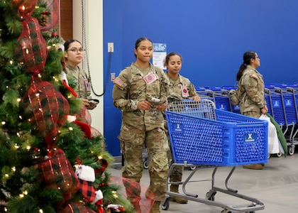 Three female Soldiers enter the Post Exchange by a Christmas Tree and pushing a shopping cart.