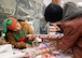 A woman dressed as an elf assists a man with wrapping a package for the holidays.