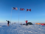 Staff members of the Ted Stevens Center for Arctic Security Studies visit Operation Ice Camp (ICE CAMP) 2024 and stand next to American and Canadian flags planted in the snow.