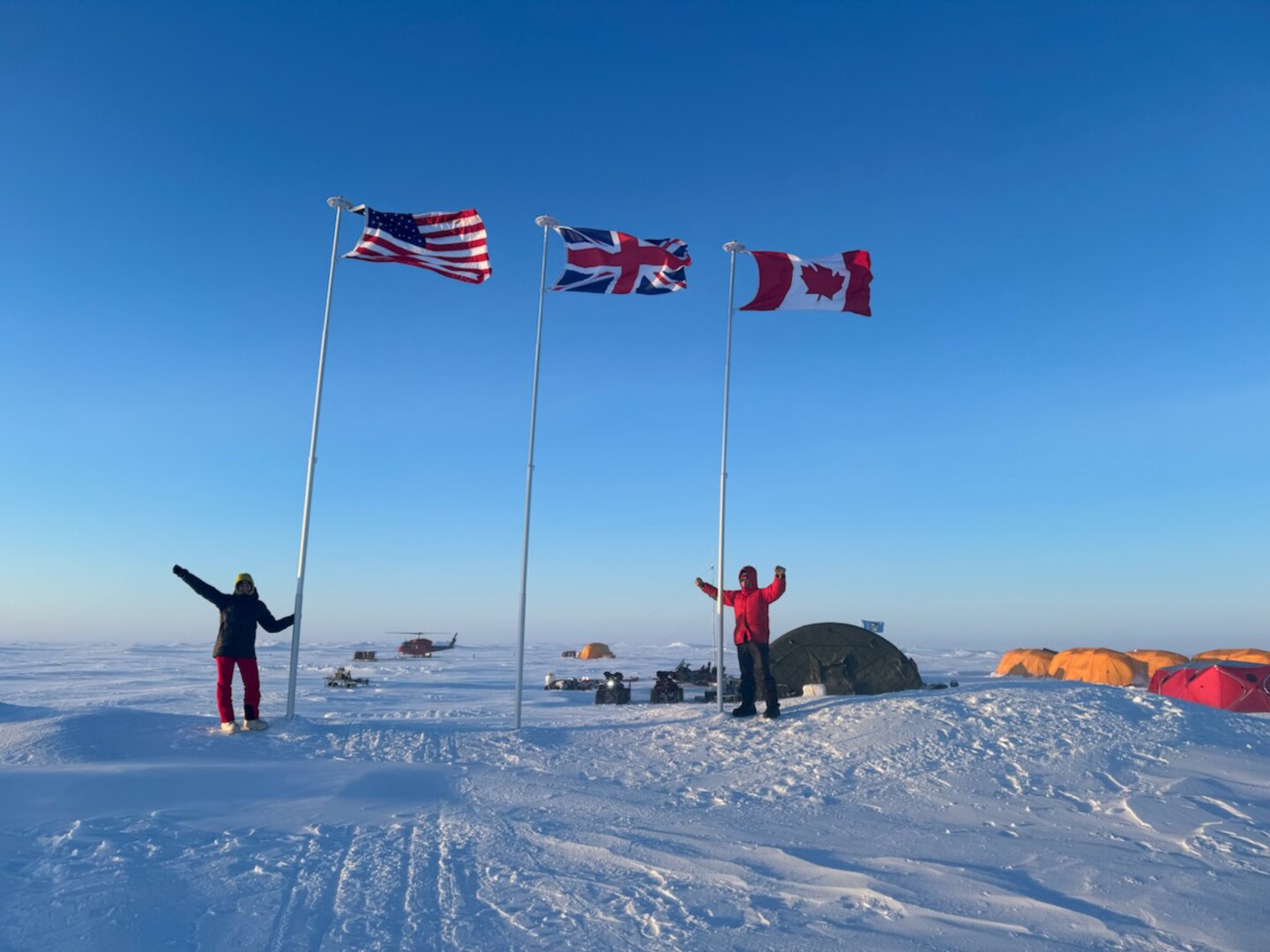 Staff members of the Ted Stevens Center for Arctic Security Studies visit Operation Ice Camp (ICE CAMP) 2024 and stand next to American and Canadian flags planted in the snow.