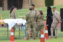 U.S. military personnel and two foreign partners stand outside around a gurney in a medical training exercise.