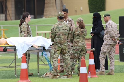 U.S. military personnel and two foreign partners stand outside around a gurney in a medical training exercise.