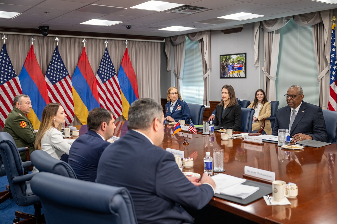 A group of government officials sit around a rectangular table with American and Armenian flags at the end of the table.