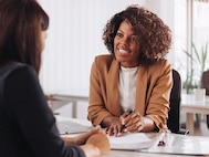 A woman at a desk reviewing a document with another woman.