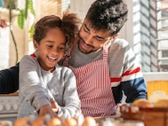 A man wearing an apron with his daughter on his lap cooking together