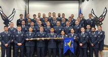 A group of Airmen in dress blues stand in formation.