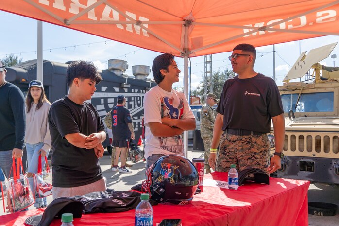 U.S. Marine Corps Sgt. Jesusaleja Arredondo, far right, a recruiter with Recruiting Sub Station Baybrook, Recruiting Station Houston, speaks to an attendee at a recruitment table display during the Houston Texans vs. Tennessee Titans football game at NRG Stadium in Houston, Texas, Nov. 24, 2024. Marines with RS Houston challenged fans with a pull-up challenge to win prizes to support the National Football League's Salute To Service game along with the other military branches. (U.S. Marine Corps photo by Sgt. Ryan H. Pulliam)