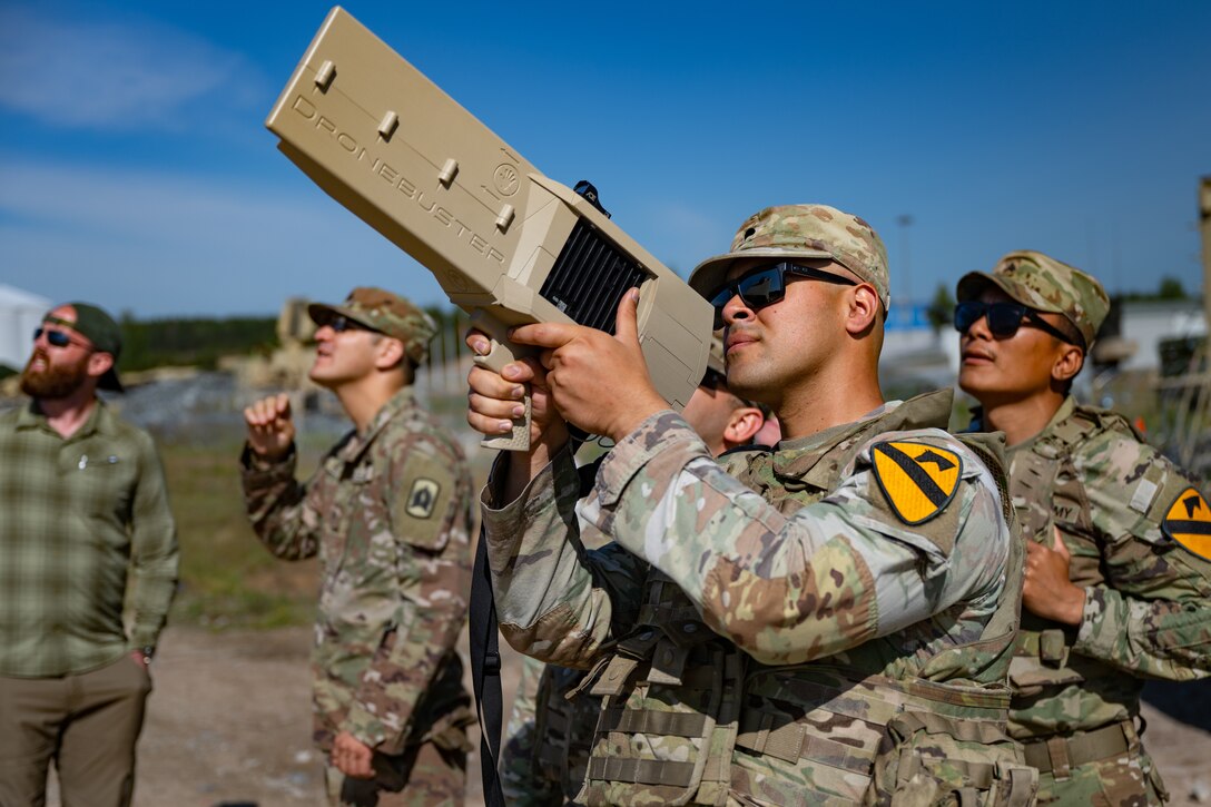 A soldier aims a device into the air. On the device's side is written "Dronebuster."