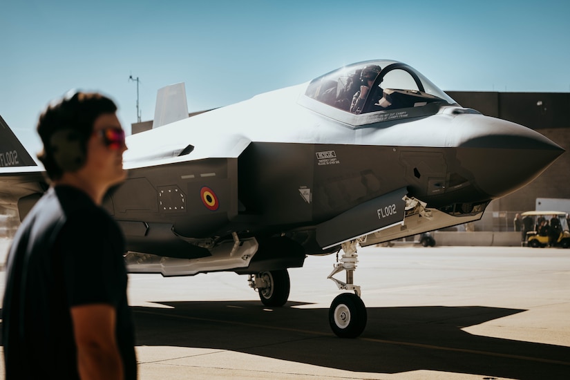 A pilot parks an aircraft on a flight line, where another person watches.