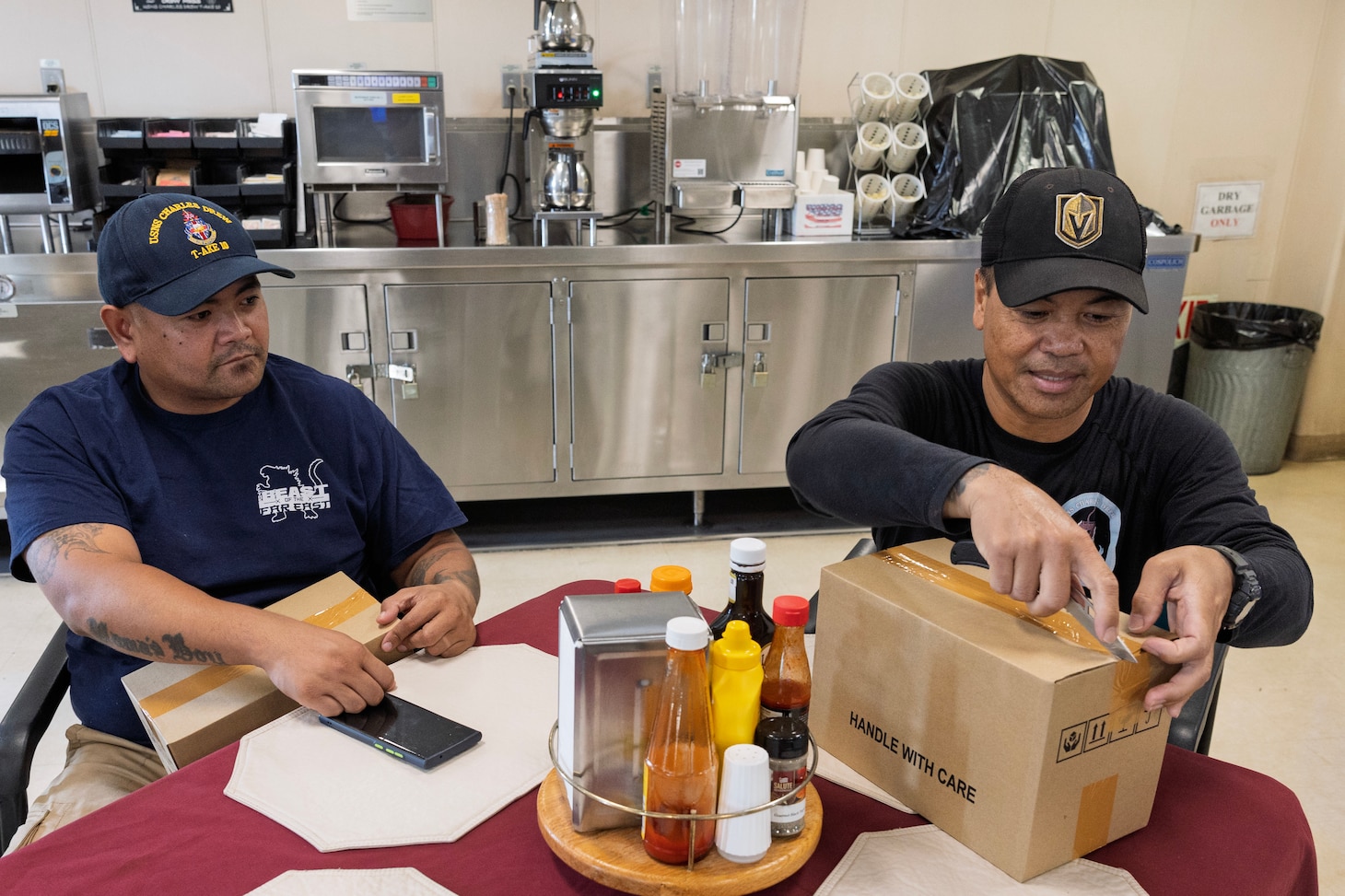 Michael Soliven, left, assistant cook, and Melvin Macaraeg, deck engineer, both with dry cargo and ammunition ship USNS Charles Drew (T-AKE 10) open a care package that was provided by the American Association of Singapore and the Stamford American International School in Singapore while aboard Charles Drew at Sembawang Wharves, Singapore, Nov. 21, 2024. (U.S. Navy photo by Grady T. Fontana)