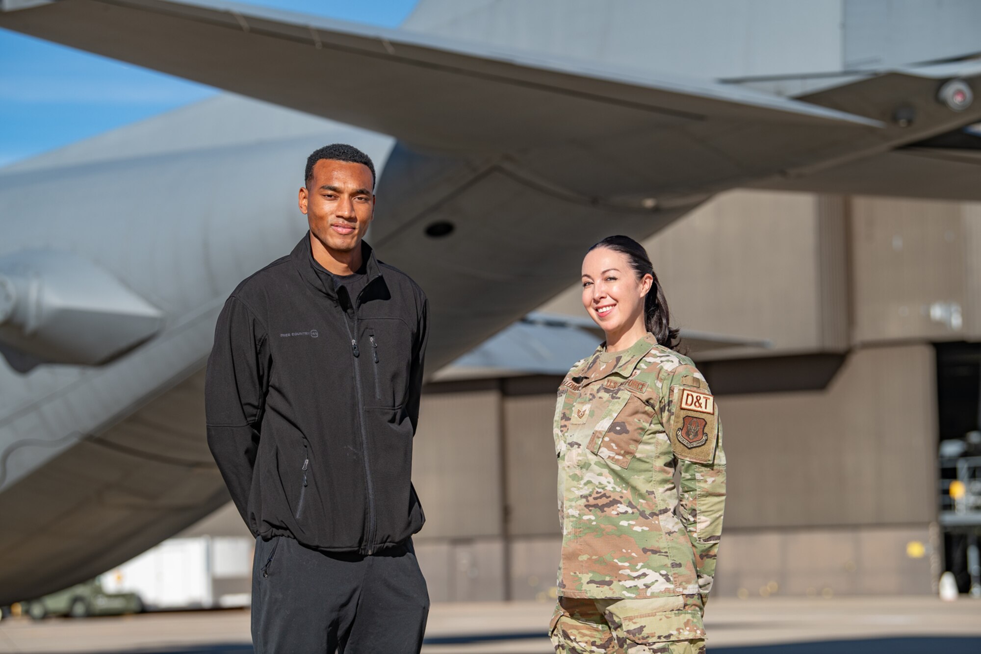 Two people stand beside a military aircraft.