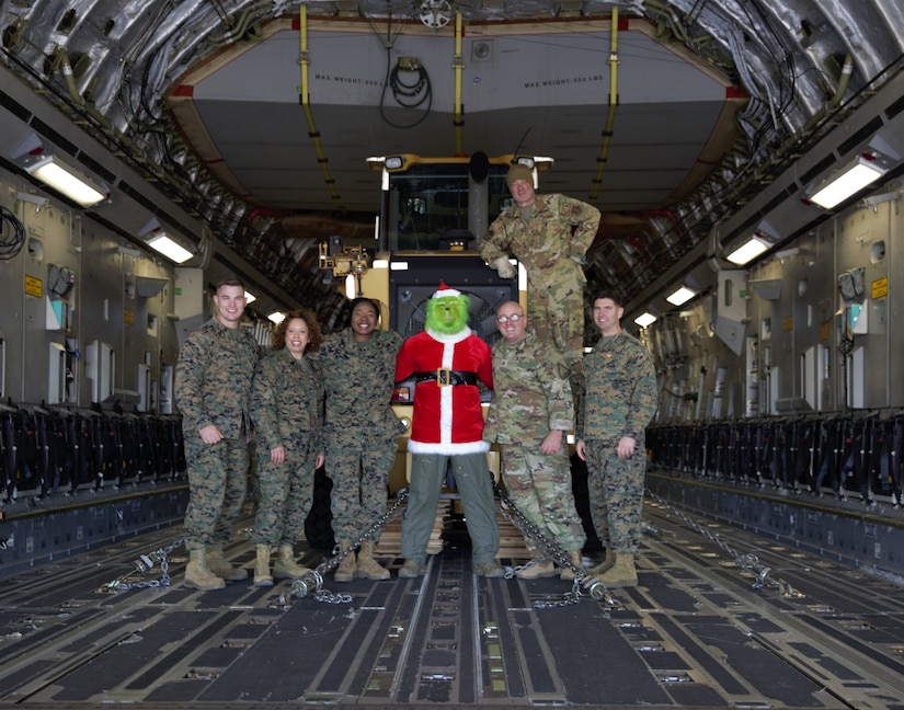 A group of service member poses for a photo with the Grinch inside the cargo hold of an aircraft.