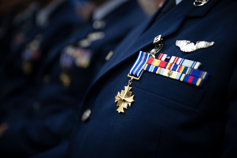 A cross-shaped medal hangs from a blue and white-striped ribbon pinned to an airman's uniform.