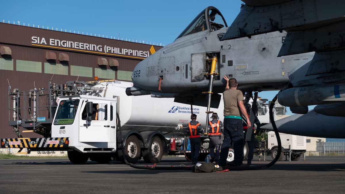 Man stands in front of fighter jet with a fuel truck nearby