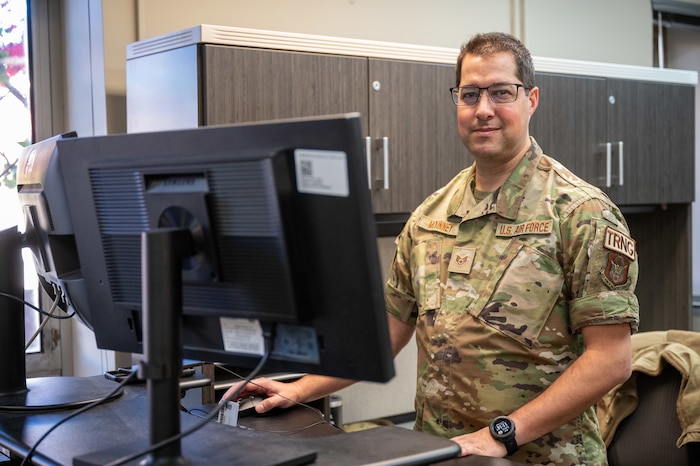 Staff Sgt. Galen McKinney stands behind his standing desk with one hand on the mouse.