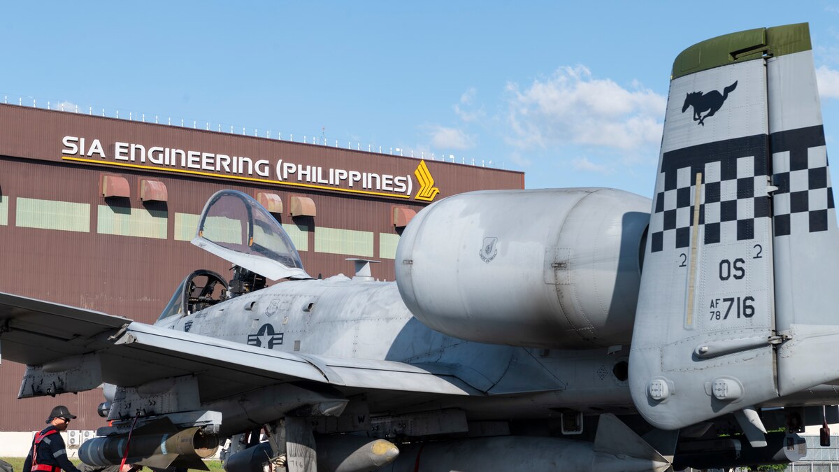 airmen work on a parked fighter jet in front of an engineering building