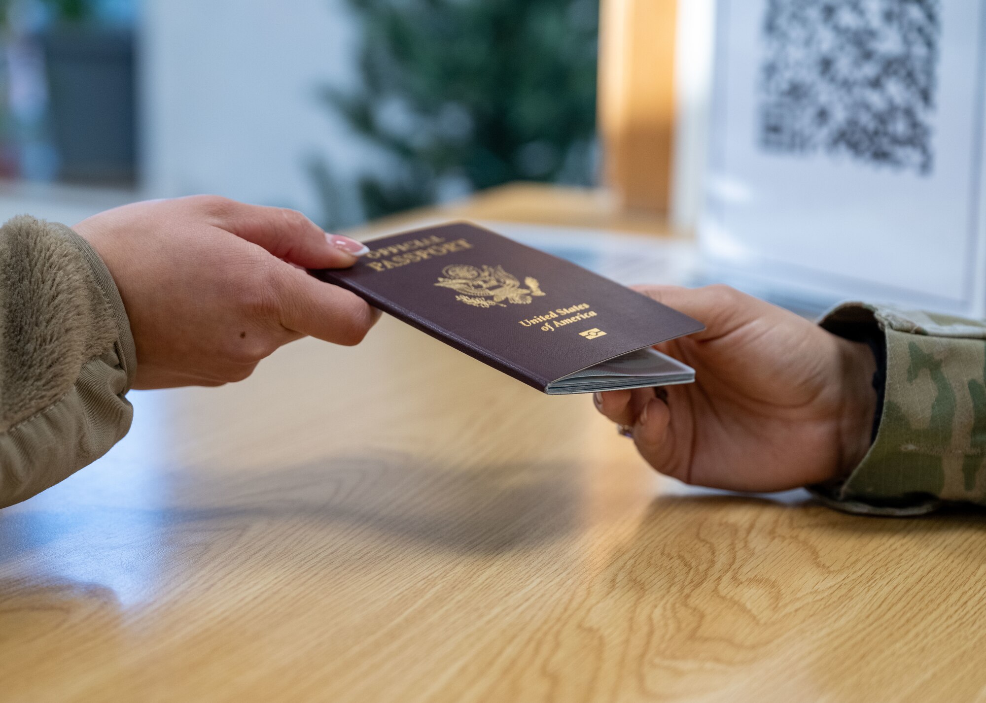 U.S. Air Force Staff Sgt. Selena Ramirez, 100th Force Support Squadron noncommissioned officer in charge of official passports, passes a customer their new official passport at Royal Air Force Mildenhall, England, Dec. 6, 2024.