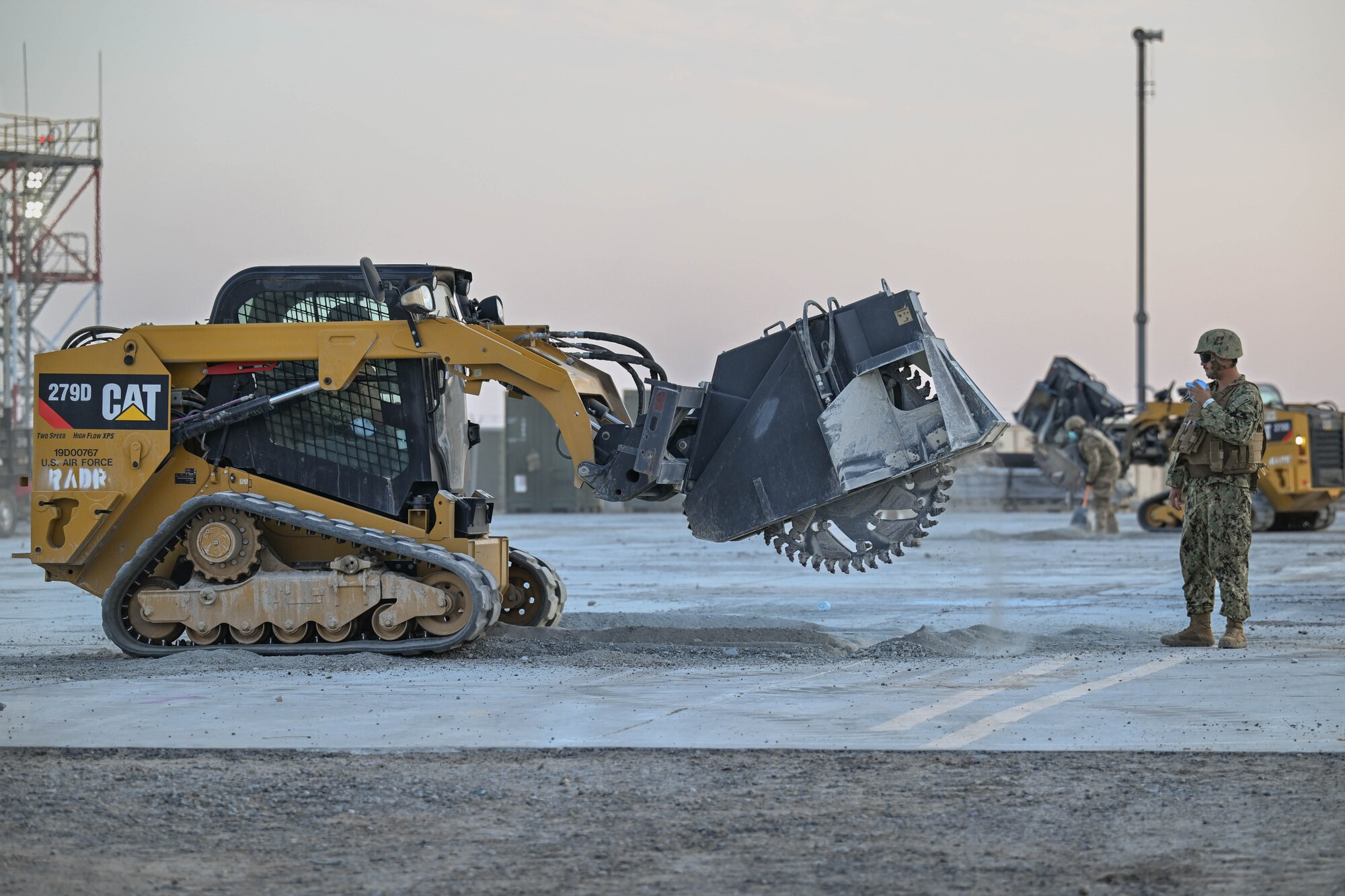 A military member looks on as another operates heavy equipment during an exercise.