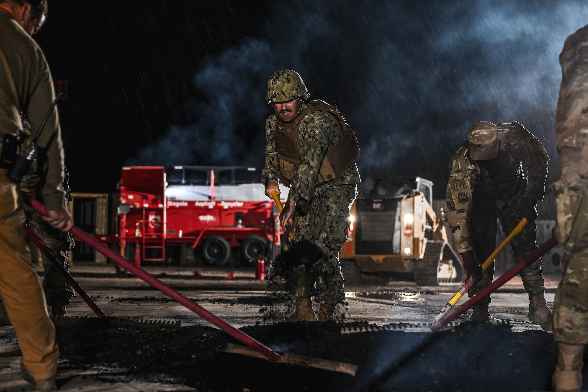 Military members shovel asphalt during an exercise.