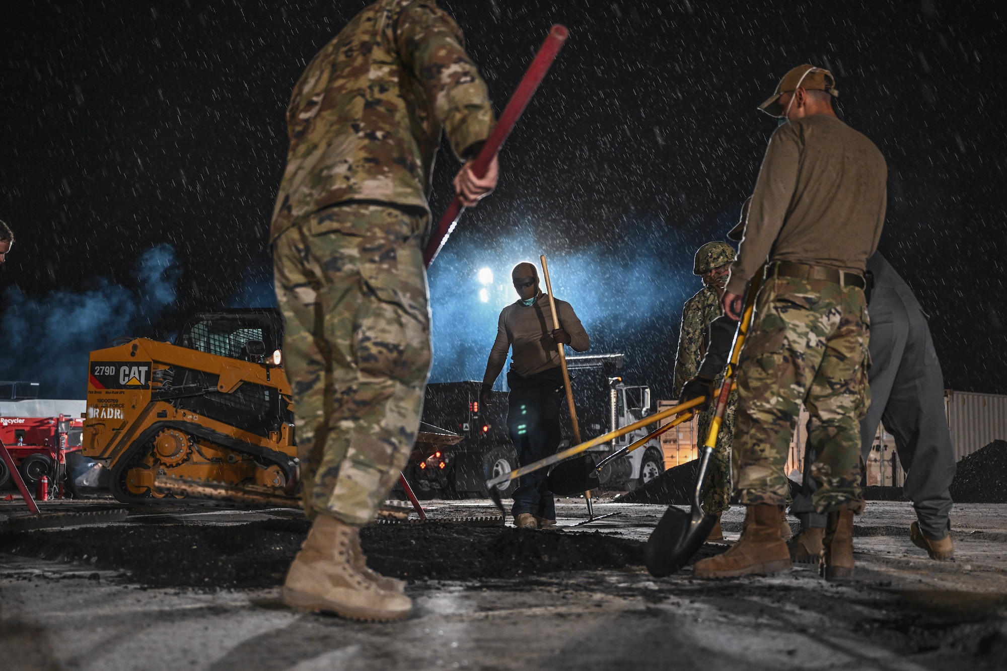 A group of Airmen shovel out asphalt during an exercise.