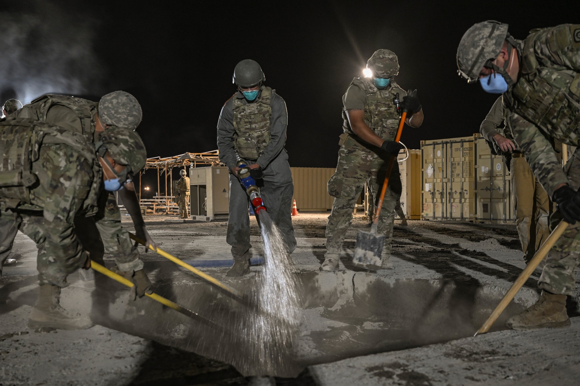 A group of military members mix concrete as one Airman sprays water.