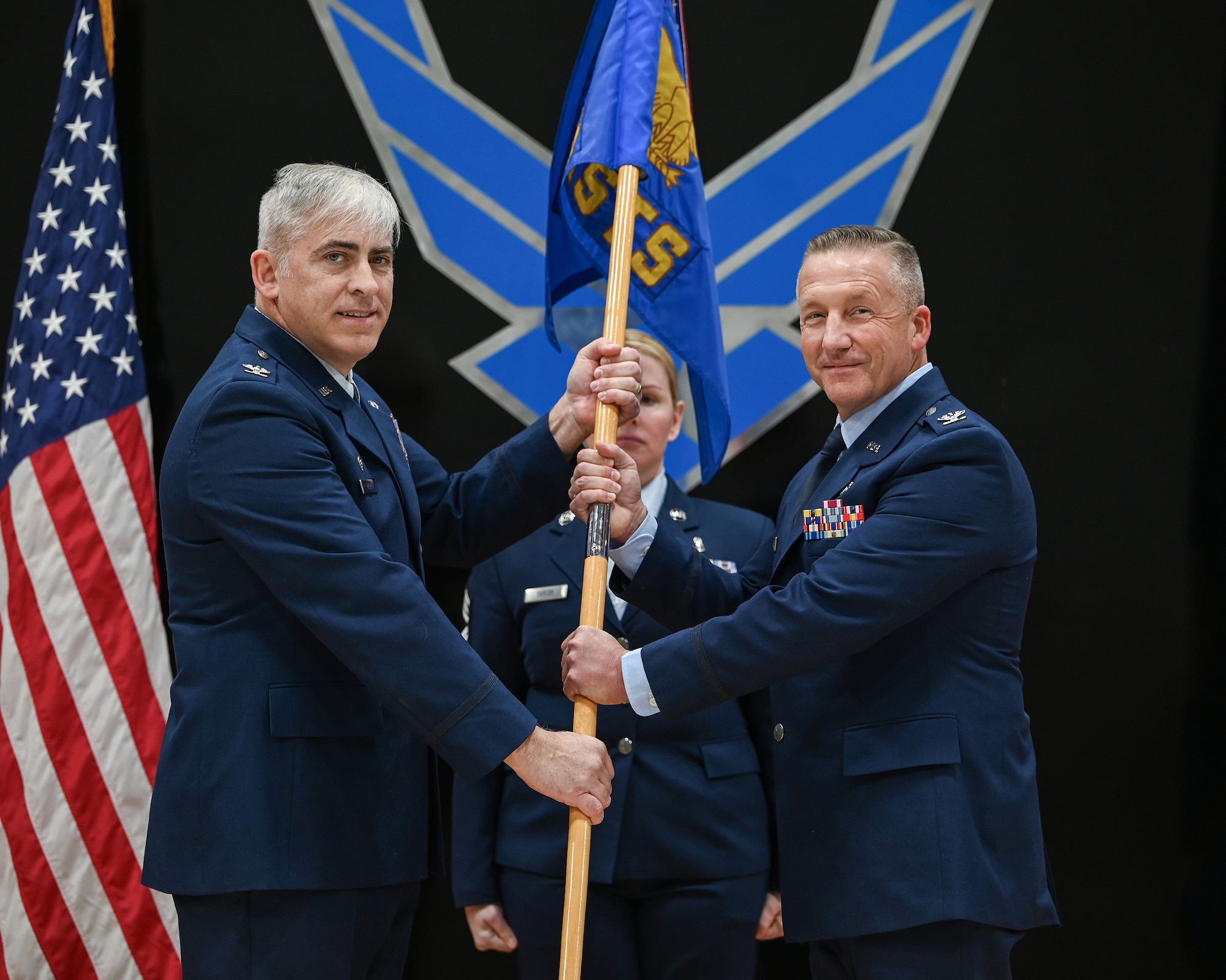 Col. Douglas Perry Jr., 445th Airlift Wing commander, passes the guidon to incoming 445th Aeromedical Staging Squadron commander, Col. Michael Policastro, during an assumption of command ceremony Dec. 7, 2024 in Hangar 4026.