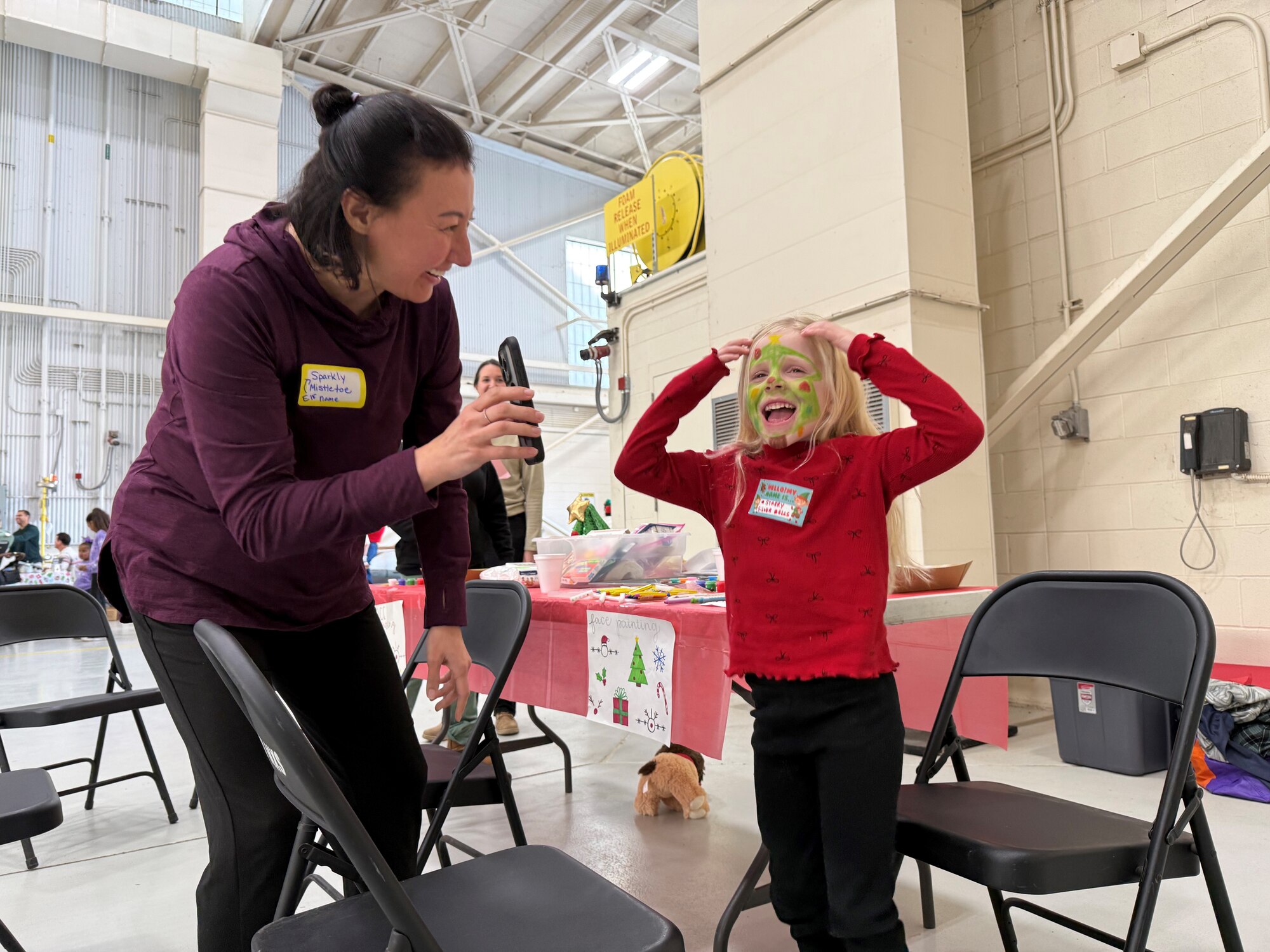 A volunteer shows a child a picture of herself after getting her face painted at the Santa on a Herc event on Dyess Air Force Base, Texas, Dec. 8, 2024. The event included photos with Santa, free toys for children, holiday games, food and face painting. (U.S. Air Force photo by Staff Sgt. Holly Cook)