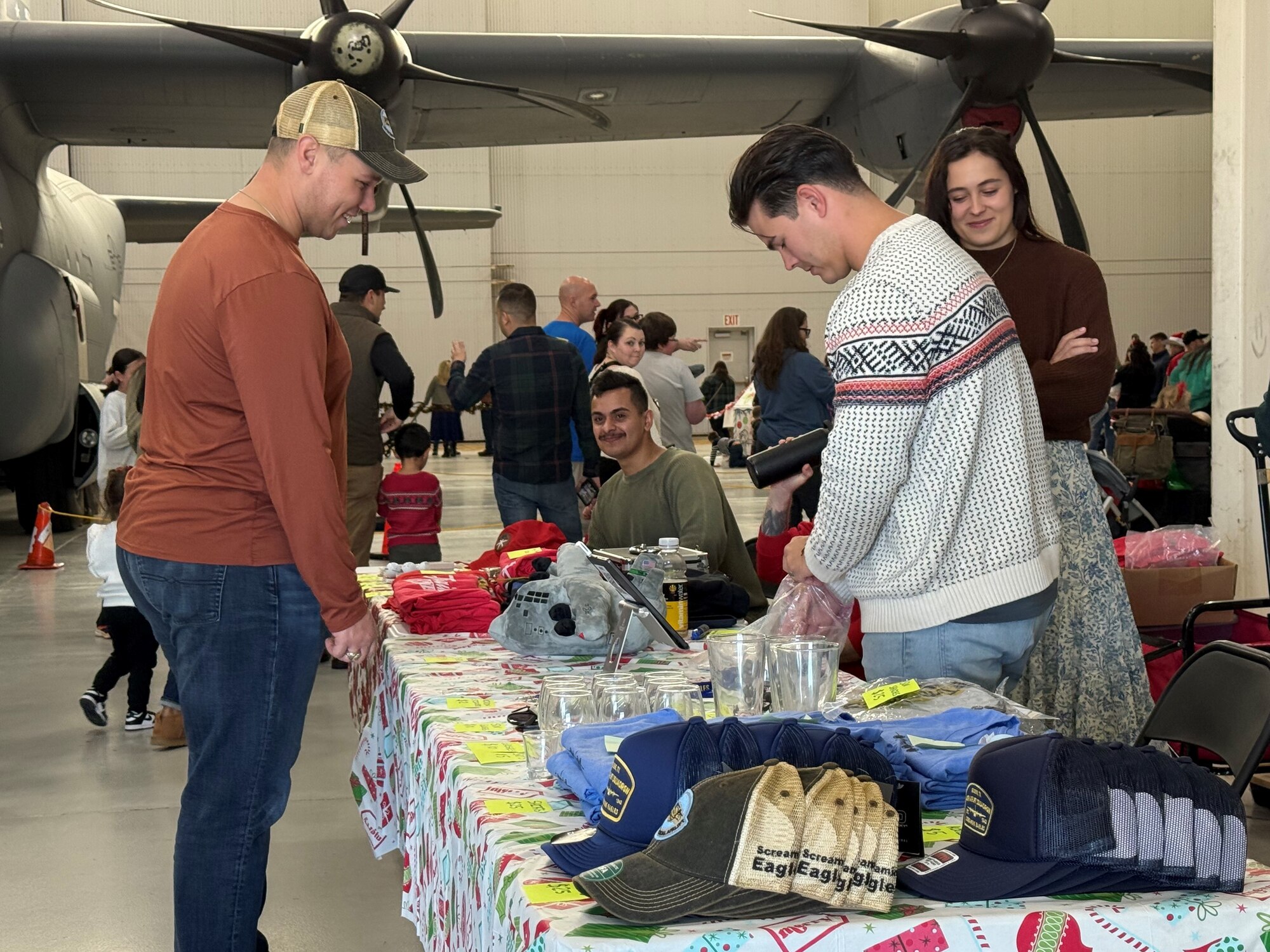 Airmen from the 317th Airlift Wing sell unit merchandise at the Santa on a Herc event on Dyess Air Force Base, Texas, Dec. 8, 2024. The 317th AW leadership hosts the event each year to give an opportunity for Airmen and their families to celebrate the holidays and all their accomplishments from throughout the year. (U.S. Air Force photo by Staff Sgt. Holly Cook)