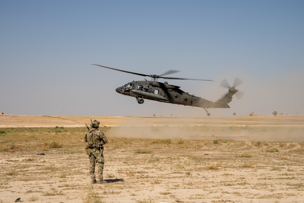 A military helicopter hovers as a service member observes.