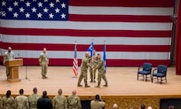 stage with American flag in the background with officers holding blue and yellow guidon in the foreground