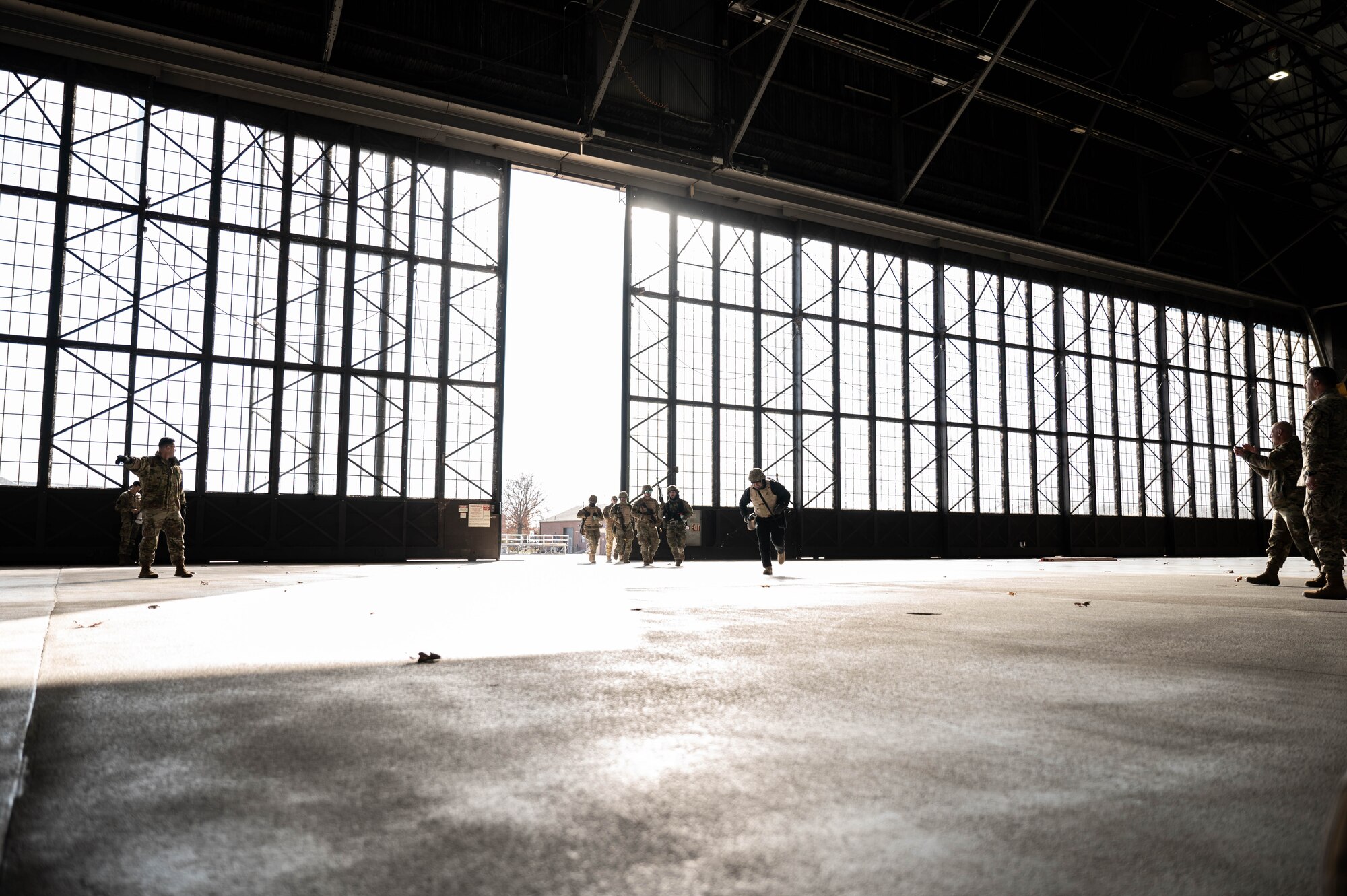 A group of airmen run through the doors of an Air Force hangar.
