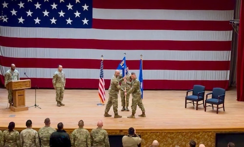 stage with American flag in the background with officers holding blue and yellow guidon in the foreground