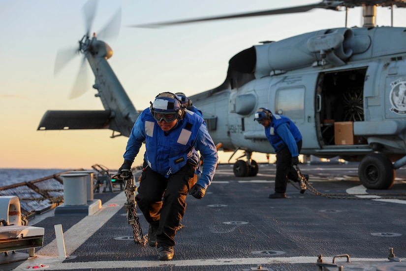 A sailor removes a chain from a helicopter on an aircraft carrier.